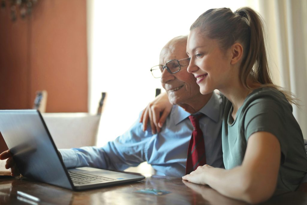 A younger woman helping an older man on the computer